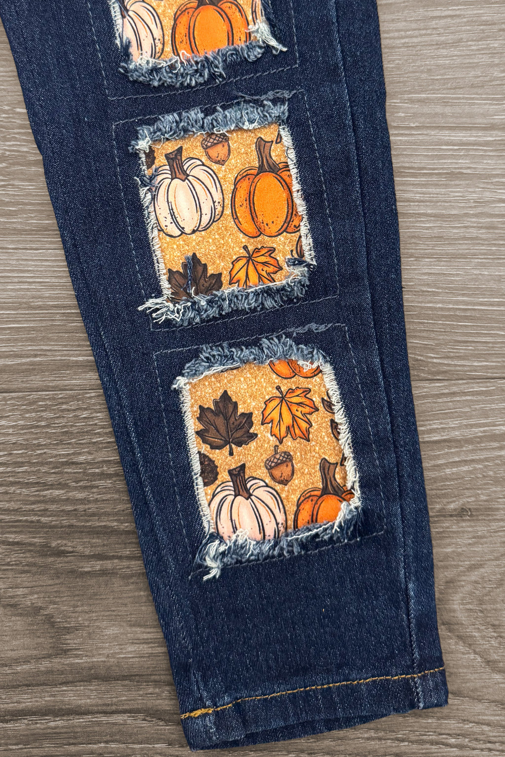 Pumpkin Denim Pant Set - 6-12 Months - Dark blue denim pant leg featuring three rectangular orange patches with pumpkin and autumn leaf prints, distressed edges.