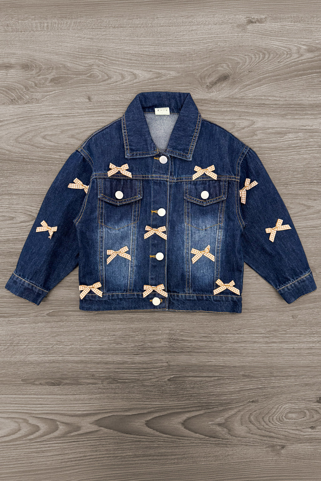 Plaid Bow Denim Jacket - 6-12 Months - Dark blue denim jacket with button front, chest pockets, and beige plaid bow appliqués on sleeves and front panels.