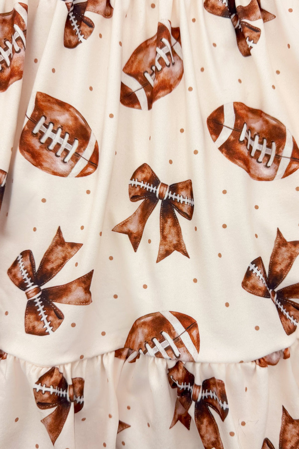 Football Bow Dress - 6-12 Months - Cream fabric dress with tan football and bow print featuring small brown polka dots.