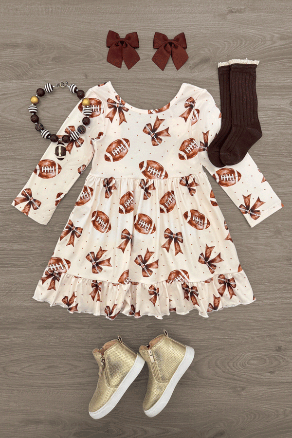 Football Bow Dress - 6-12 Months - Cream long-sleeve dress with football and bow prints, ruffled hem, paired with brown socks, gold sneakers, and maroon bow.