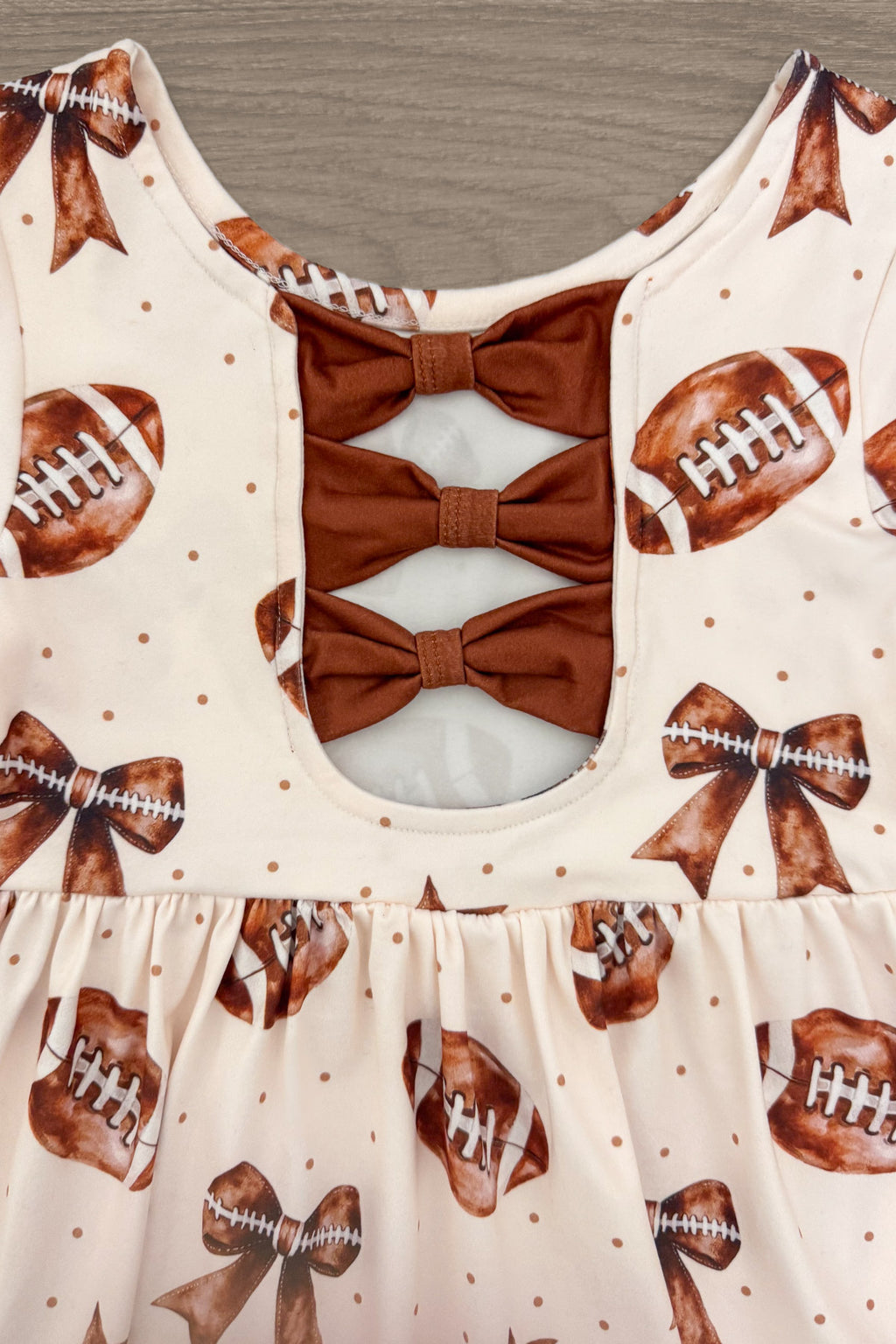 Football Bow Dress - 6-12 Months - Cream dress with football and bow prints, featuring three tan fabric bows down an open back cutout.