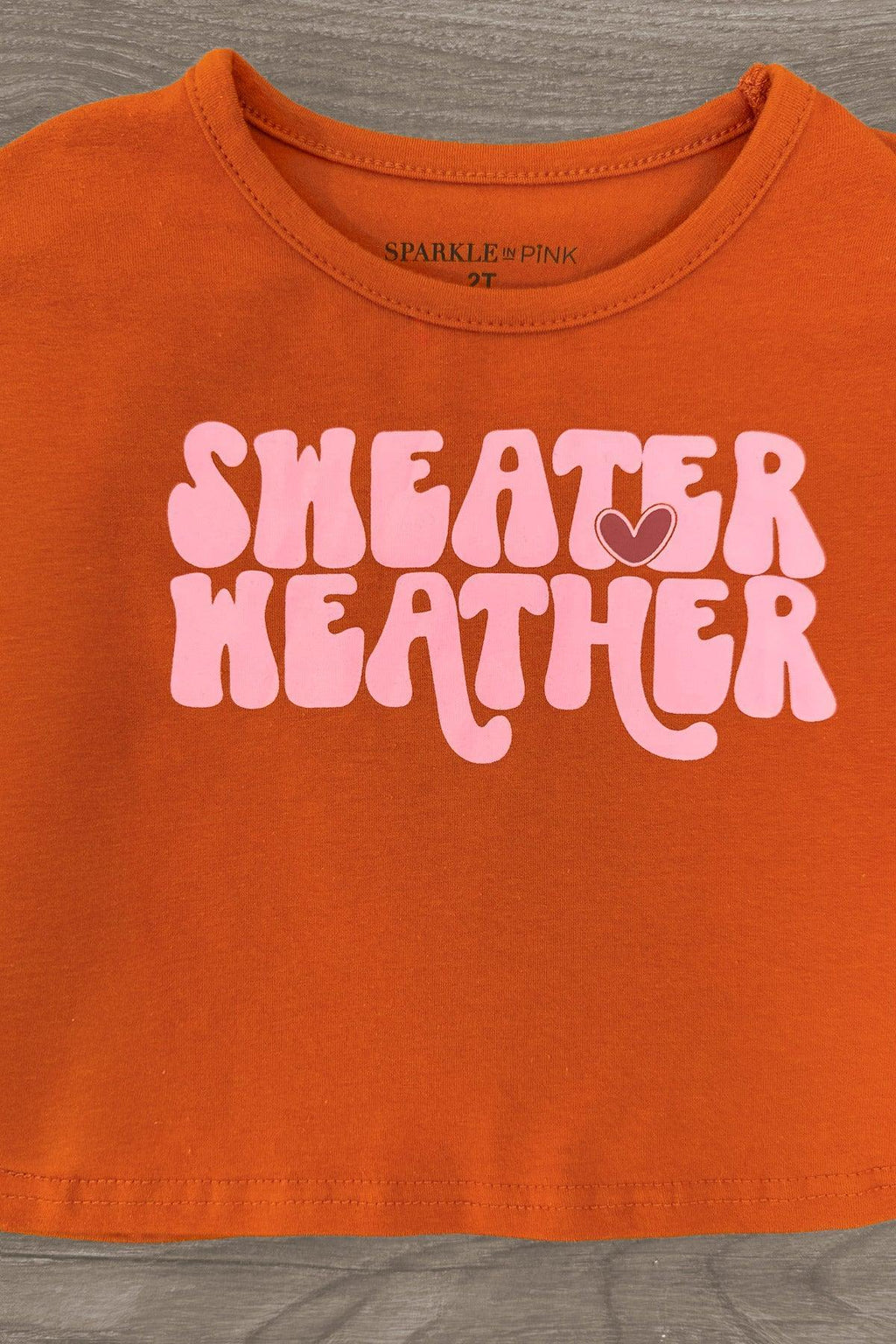 "Sweater Weather" Denim Bell Bottom Set - 6-12 Months - Rust-colored cropped denim top with rounded neckline and pink "Sweater Weather" text in bold retro font.