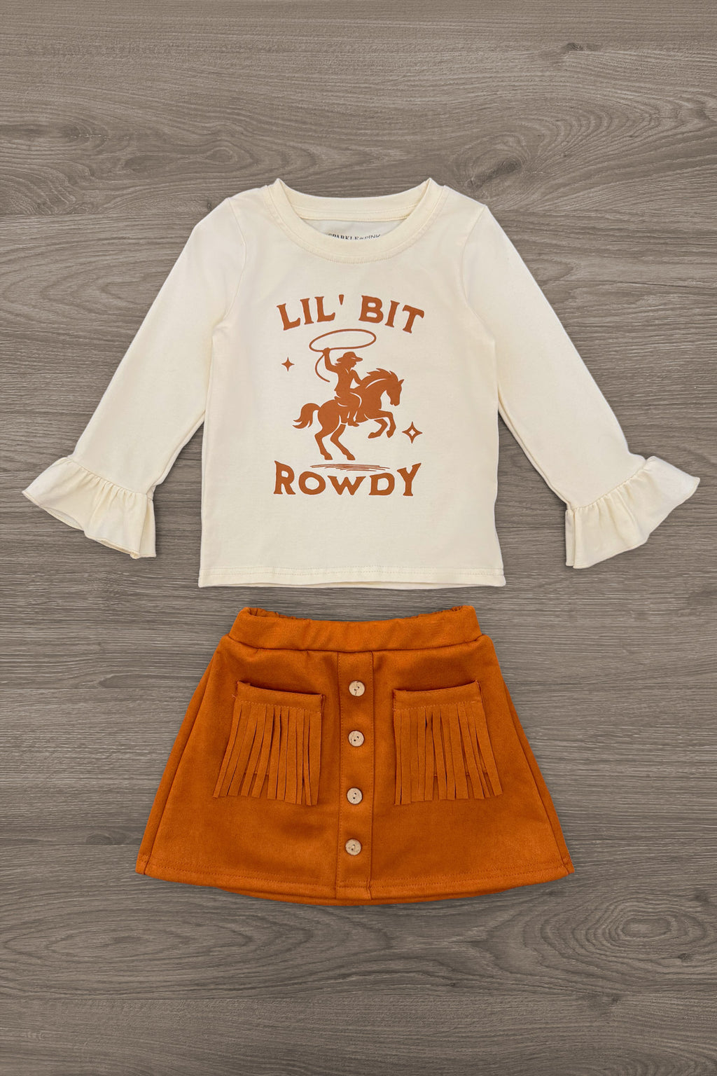 "Lil' Bit Rowdy" Suede Skirt Set - 6-12 Months - Cream long-sleeve top with rust graphic and ruffled cuffs paired with rust-orange suede button-front skirt.