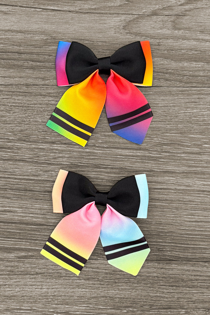 Crayon Trendy Bows - RAINBOW! - Bright Rainbow - Black bow with bright rainbow-colored ends and two black stripes on each tail against a wood background.