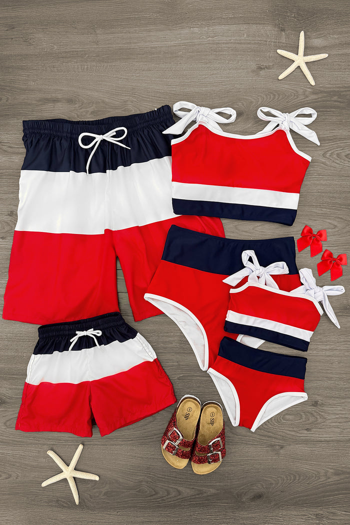Red, white, and navy blue striped matching family swimsuits with bow tie straps and swim trunks on wooden floor.