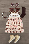 "Game Day" Football Bow Dress - 6-12 Months - Cream dress with brown football and pink bow prints, brown bow straps, paired with brown socks, tan boots, brown bow hair.