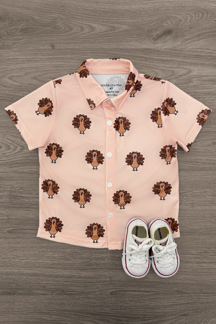 Turkey Button Down Top - 6-12 Months - Light pink short-sleeve button-down top with repeating turkey prints and a pointed collar, styled with white sneakers.