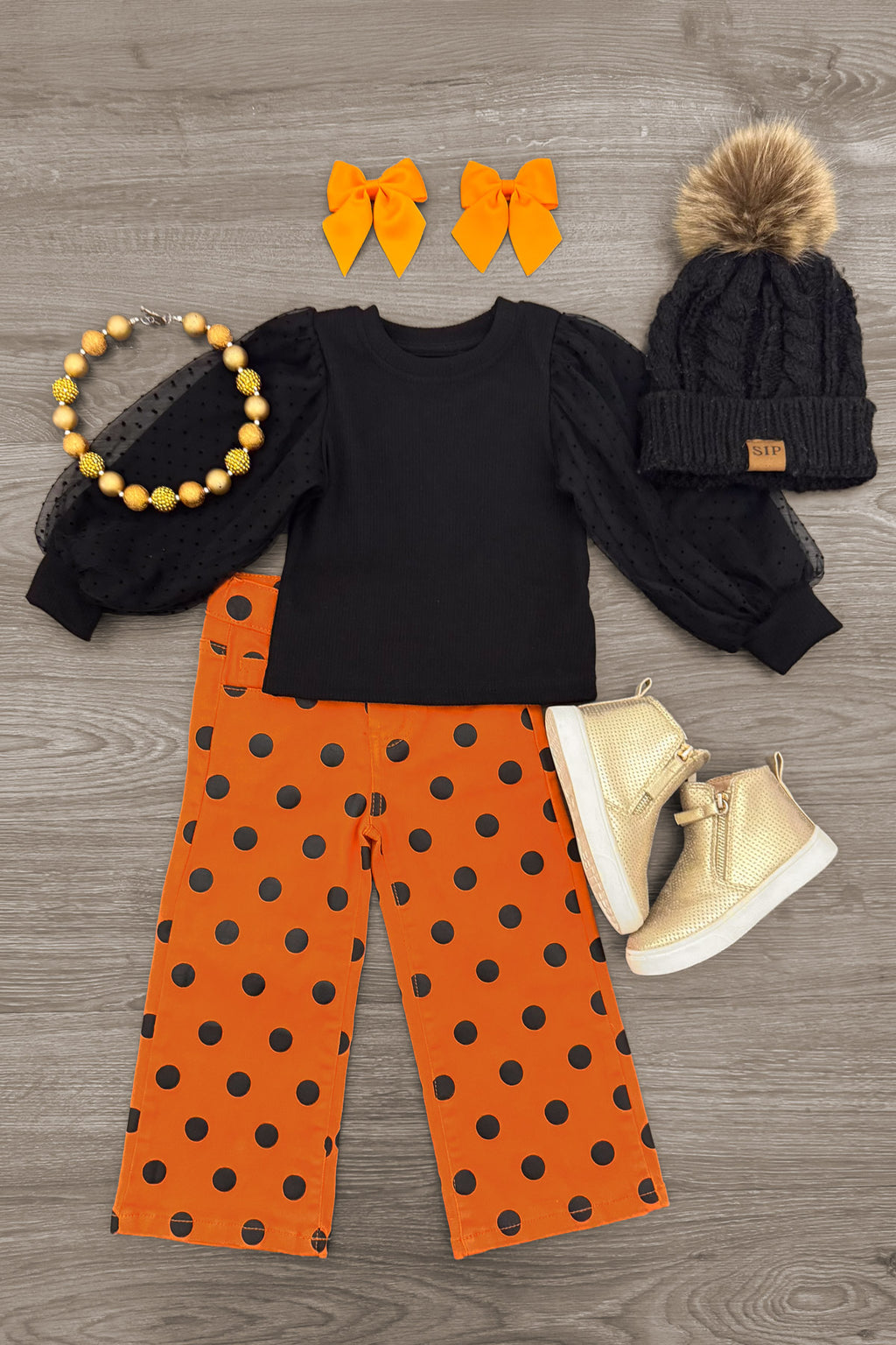 Black & Orange Polka Dot Denim Pant Set - 6-12 Months - Black long-sleeve top paired with orange polka-dot denim pants, knit beanie, orange bows, necklace, and cream boots.