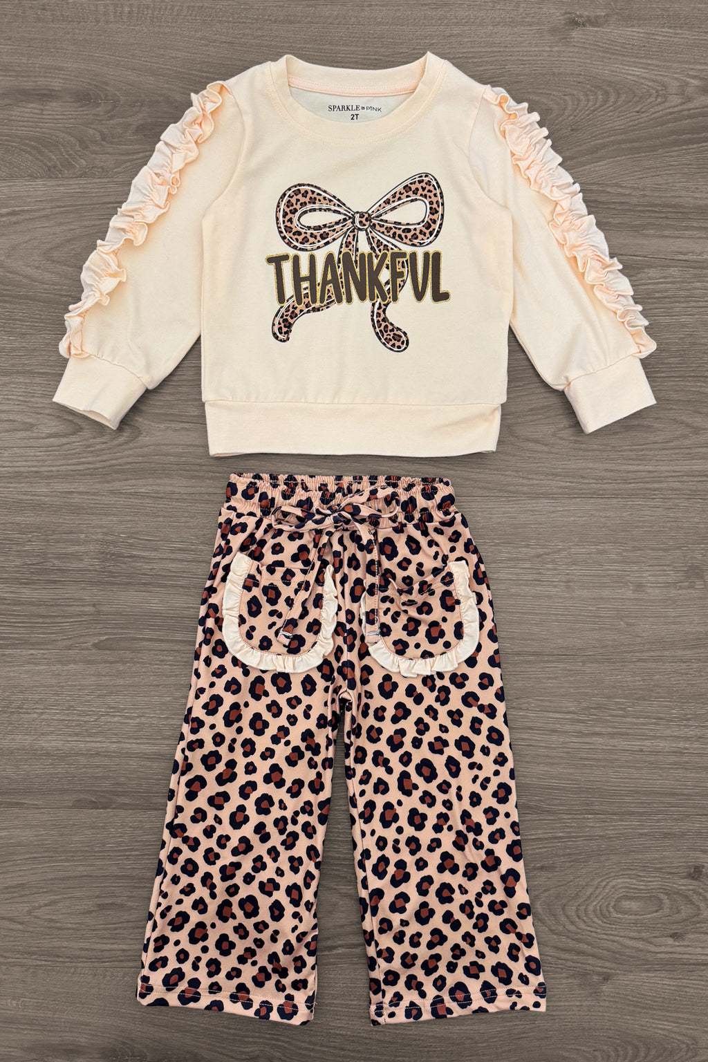 "Thankful" Cheetah Bow Pant Set - 6-12 Months - Cream long-sleeve top with ruffled sleeves and "Thankful" cheetah print bow graphic paired with cheetah print wide-leg pants.