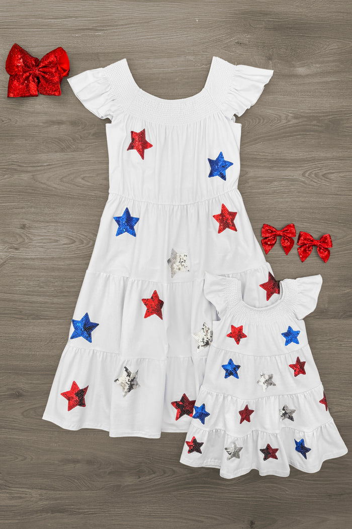 Mom & Me - Sequin Star Ruffle Dress - 6-12 Months - White sequin star ruffle dress with red and blue stars, styled in adult and child sizes with matching red bow accessories.