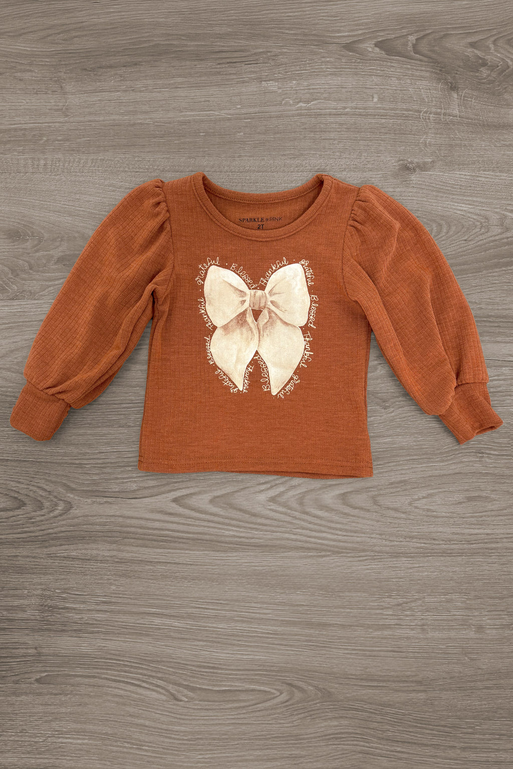 "Grateful, Blessed, Thankful" Plaid Pant Set - 6-12 Months - Rust long-sleeve toddler top with a large cream bow graphic and gathered sleeves.