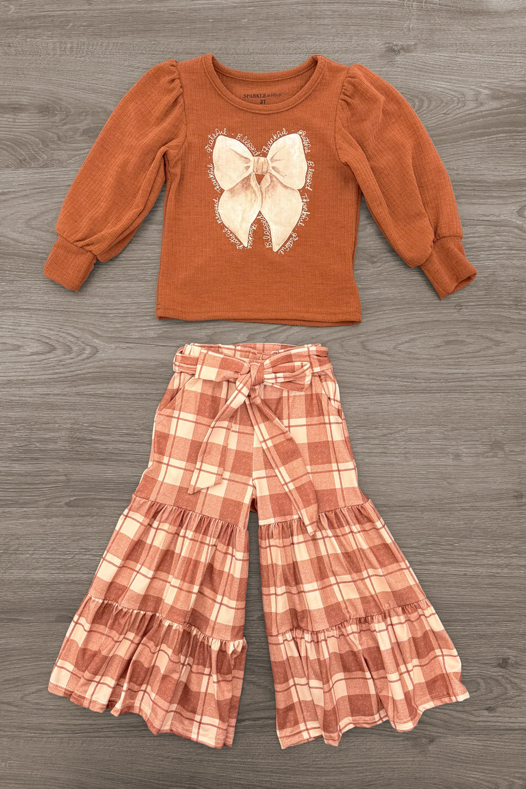 "Grateful, Blessed, Thankful" Plaid Pant Set - 6-12 Months - Rust long-sleeve shirt with a cream bow graphic paired with wide-leg rust, cream, and white plaid pants.