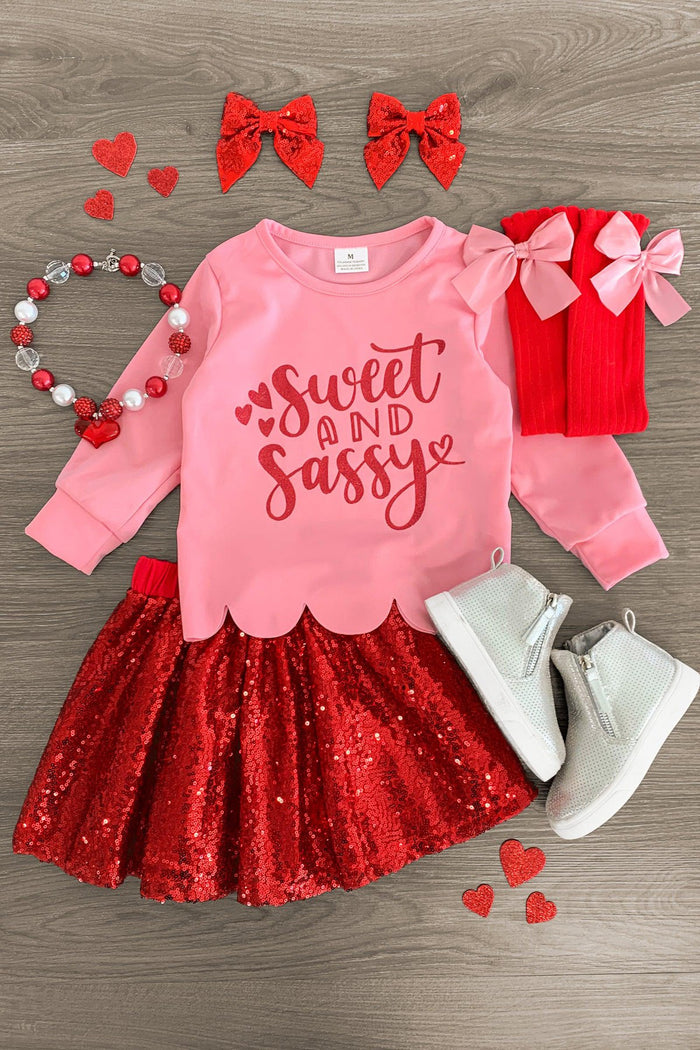 "Sweet & Sassy" Red Sequin Skirt Set - 3XS-6-12 Months - Pink long-sleeve shirt with red "Sweet and Sassy" text, red sequin skirt, red and pink bows, white boots, and heart necklace.