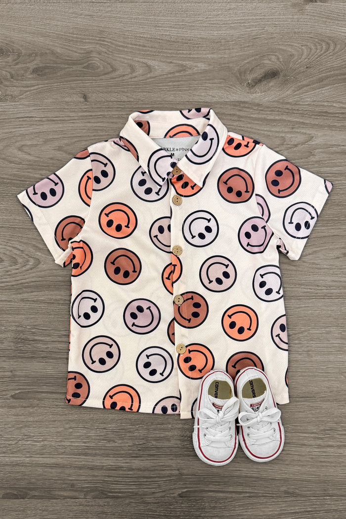 Pastel Smiley Face Button Down Top - 3XS-6-12 Months - Tan button-down shirt with colorful pastel smiley faces and pair of white baby sneakers on wooden floor.