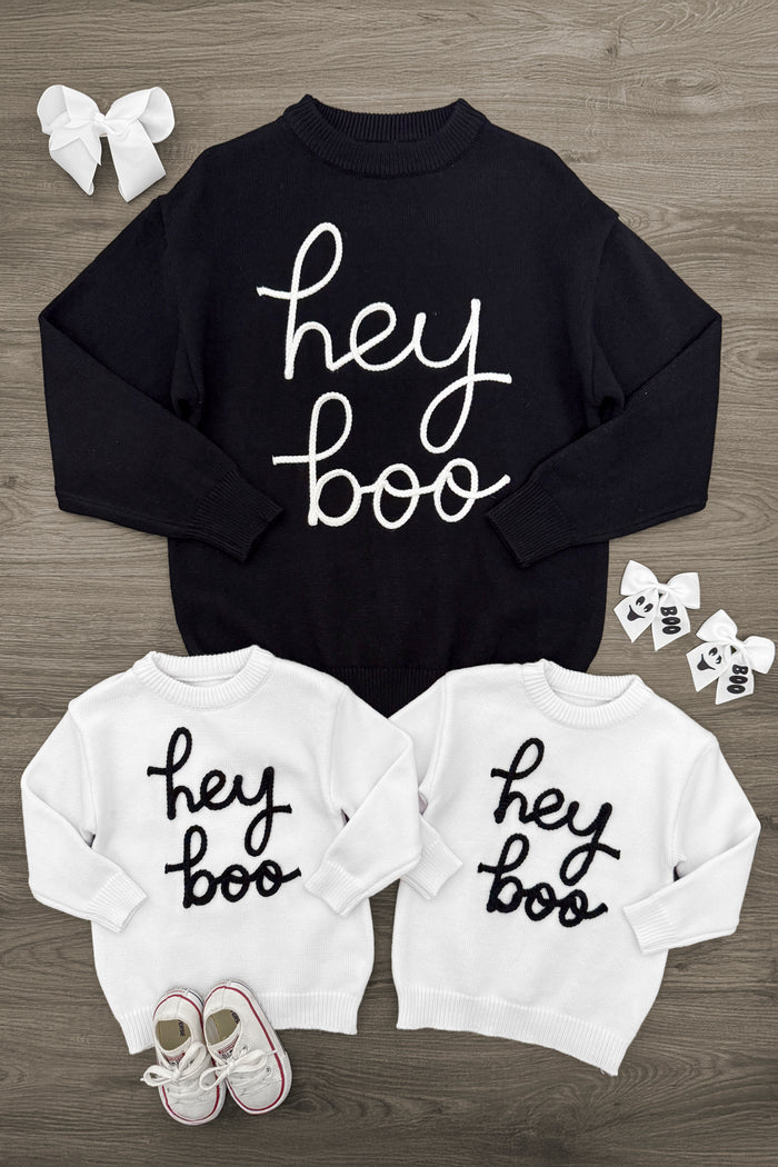 Mom & Kid - "Hey Boo" Sweater - CHILD-3XS-6-12 Months - Black adult sweater and two white kid sweaters with "hey boo" script, displayed flat on wood floor with baby shoes and bows.