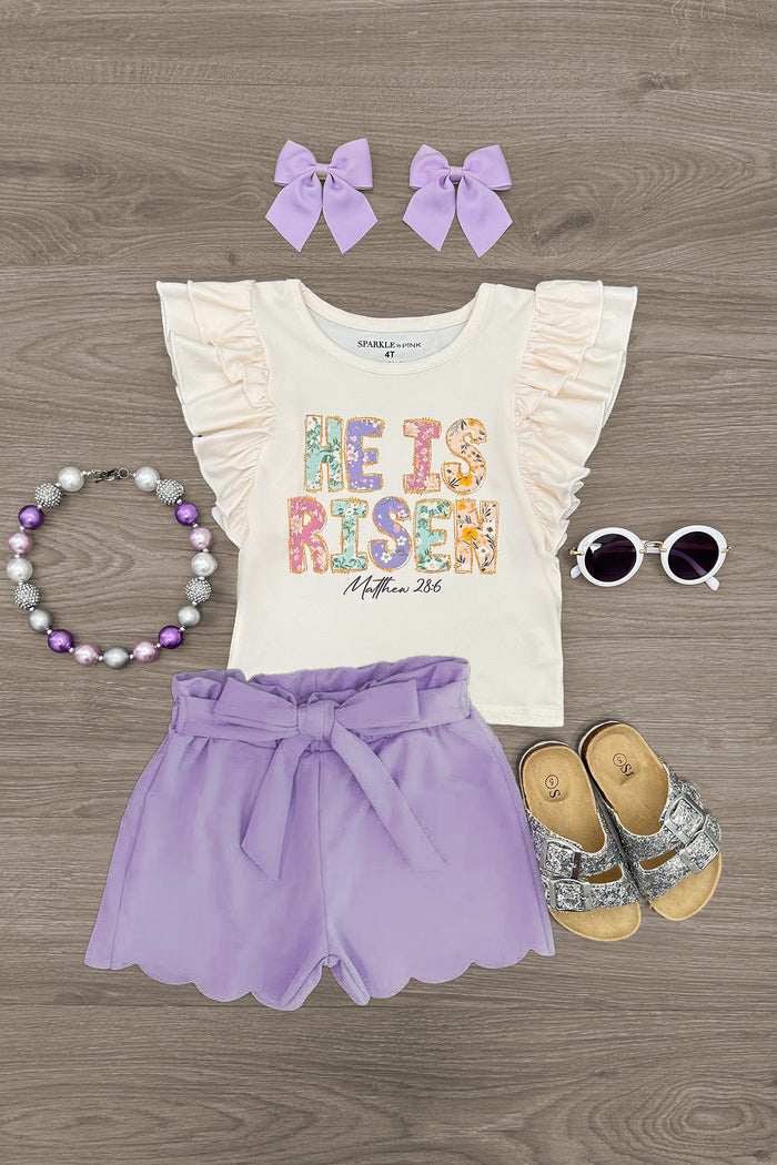 "He Is Risen" Lavender Short Set - 6-12 Months - Cream ruffle-sleeve top with colorful "He Is Risen" text, lavender shorts with bow, matching bows, necklace, sunglasses, and .