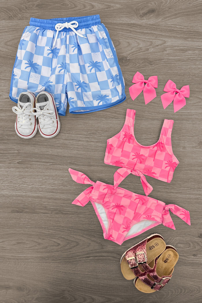 Blue and white checkered swim trunks with white drawstring, pink checkered two-piece swimsuit, pink hair bows, white.