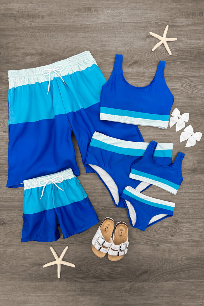 Set of blue striped family swimsuits with gradient navy to light blue shades, including shorts and various bikini tops.