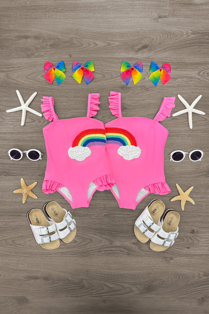Pink Rainbow BFF Swimsuit - Left Side / 6-12 Months - Matching pink toddler swimsuits with rainbow patches, ruffled shoulder straps, paired with white sandals and rainbow hair.