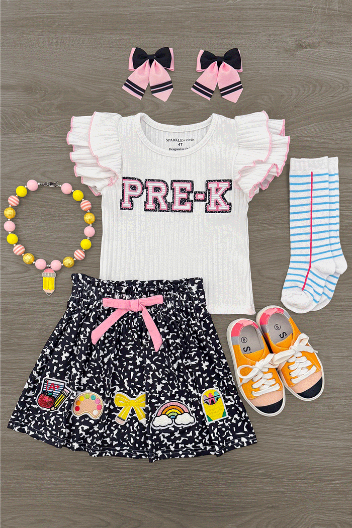 "Pre-K - Sixth Grade" Notebook Skirt Set - PRE-K / 2T - White ruffled sleeve top with "PRE-K" text, black floral skirt with pink bow, striped socks, orange sneakers, pink bow hair.