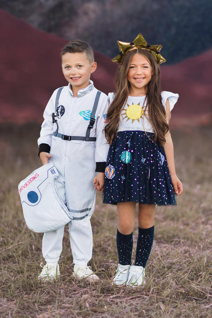 Space Kid Costumes - Space Girl / 3XS-6-12 Months - Boy in white astronaut costume with helmet prop and girl in navy space-themed dress with sun headband and knee-high socks.