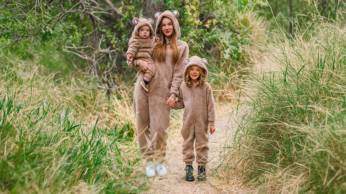 Mom and two children wearing matching brown bear costumes while walking together on a wooded trail.
