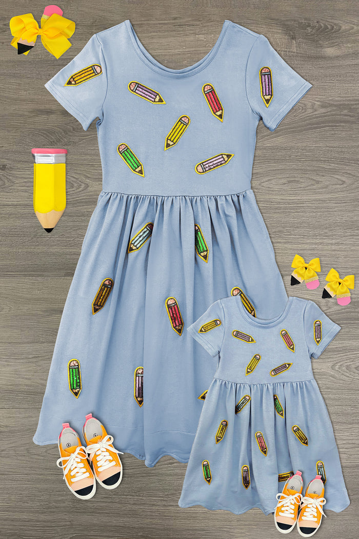 Flat lay of matching light blue adult and child Blue Pencil Dresses with colorful sequin pencil appliqués.