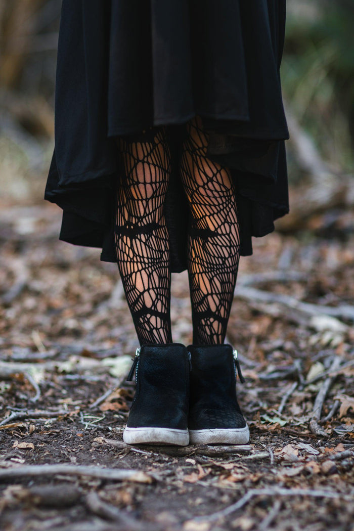 Black Vampire Queen Tights - XXS-12-18 Months - Black tights with intricate spider web pattern worn with a black skirt and black boots on woodland ground.