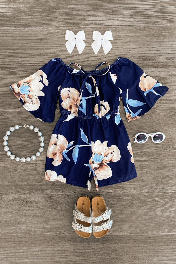 Navy Floral Bell Sleeve Romper - 3XS-6-12 Months - Navy romper with large beige floral print, bell sleeves, front tie, paired with white bow hair clips, pearl bracelet, white.