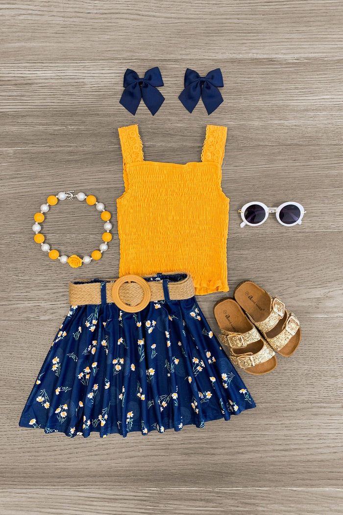 Mustard & Navy Daisy Skirt Set - 6-12 Months - Mustard yellow sleeveless top with navy blue daisy skirt, matching navy bow clips, beaded necklace, white sunglasses, and.