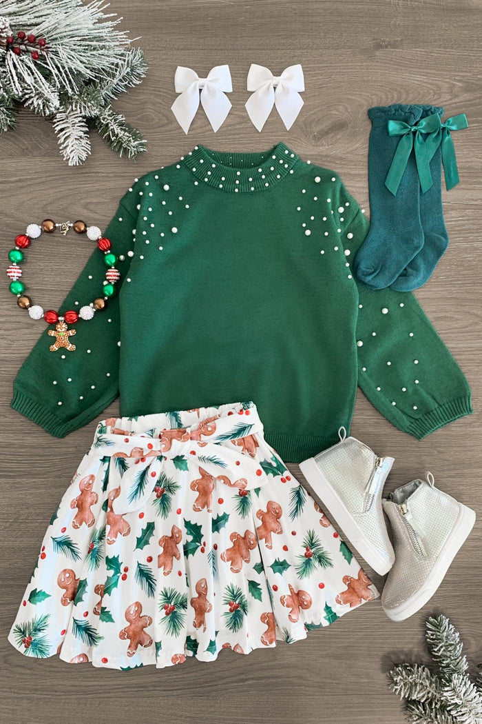 Holly Gingerbread Pearl Skirt Set - 3XS-6-12 Months - Green long-sleeve sweater with pearl accents, white skirt with gingerbread print, white boots, green socks with bows, two.
