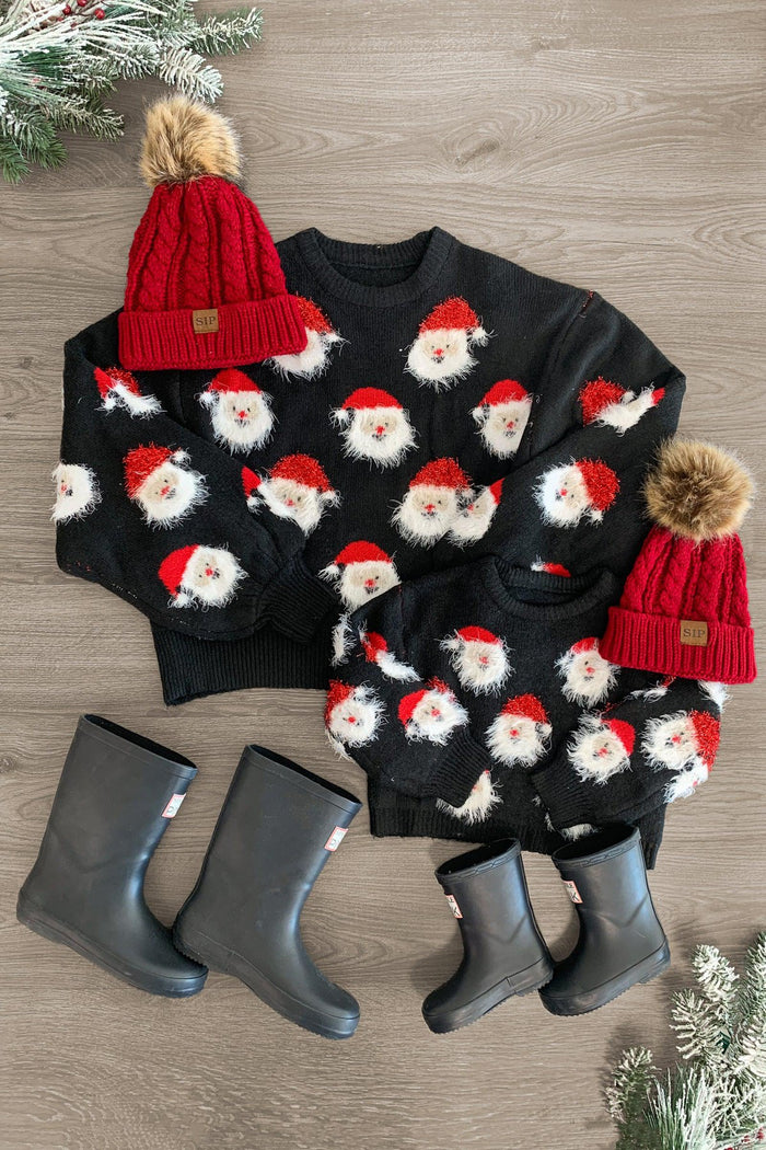 Mom & Me - Fuzzy Happy Santa Sweater - CHILD-3XS-6-12 Months - Black fuzzy sweaters with repeated happy Santa faces, paired with red knit hats with pom-poms and gray rain boots on wood.