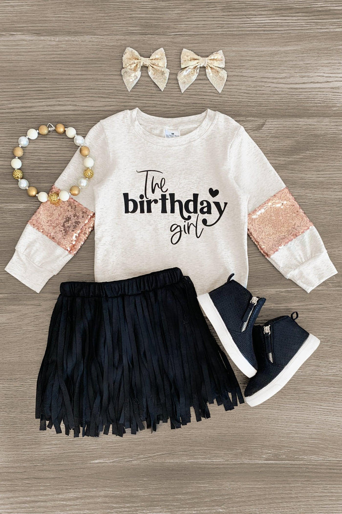 "The Birthday Girl" Sequins & Fringe Suede Skirt Set - 3XS-6-12 Months - Cream long-sleeve shirt with rose gold sequin sleeves and "The birthday girl" text, black fringe suede skirt, navy high-top.