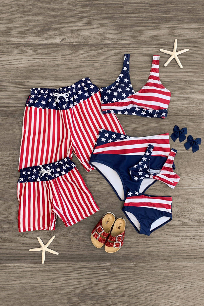Red, white, and navy abstract American flag swimsuits set with stars and stripes, including women's bikini, boys' trunks,.