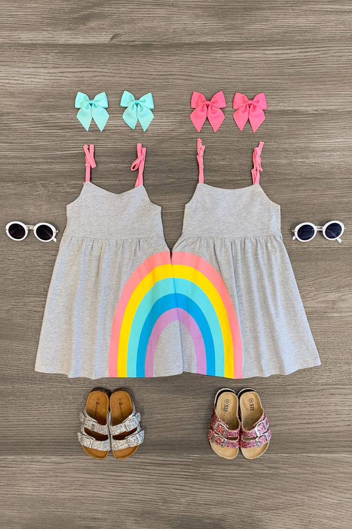 Best Friends Gray Rainbow Dress - Left Side / 3XS-6-12 Months - Two gray sleeveless dresses with colorful rainbow stripes at the bottom, paired with matching bows and sandals, laid on.