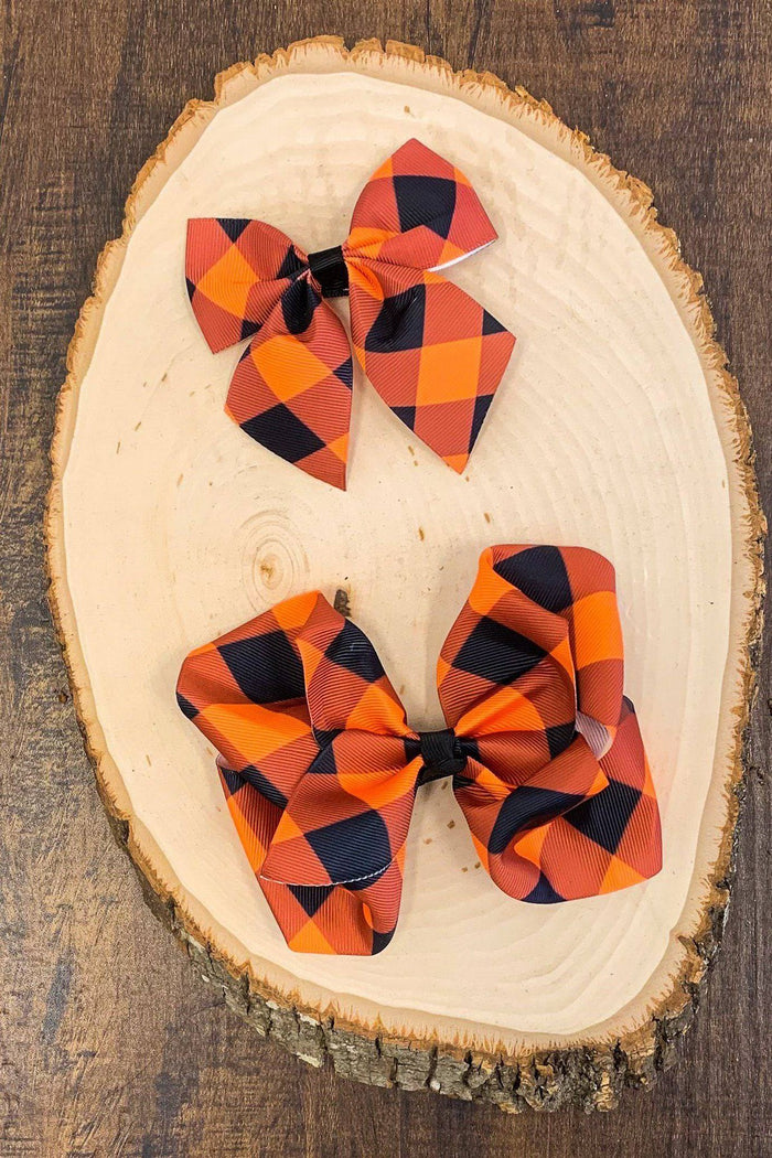 Black & Orange Plaid Bows - 3 inches - Two black and orange plaid bows, one 3-inch and one 6-inch, displayed on a wood slice.