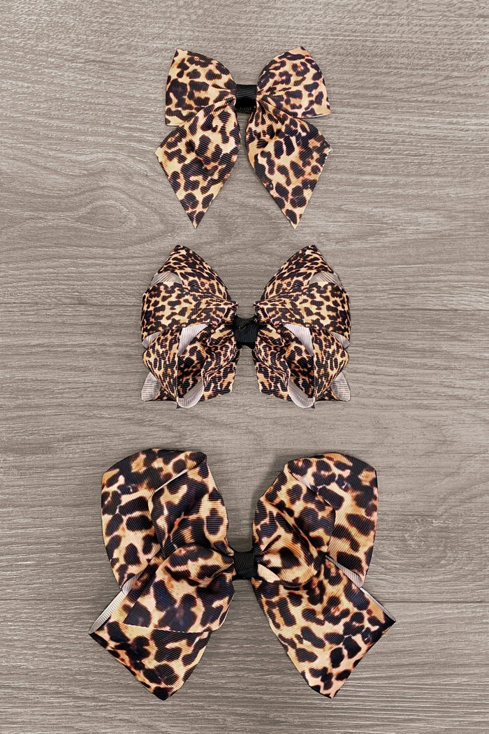 Cheetah Bows - 3 inches - Three pairs of leopard print fabric bows in 3, 4, and 6-inch sizes arranged vertically on a wood surface.