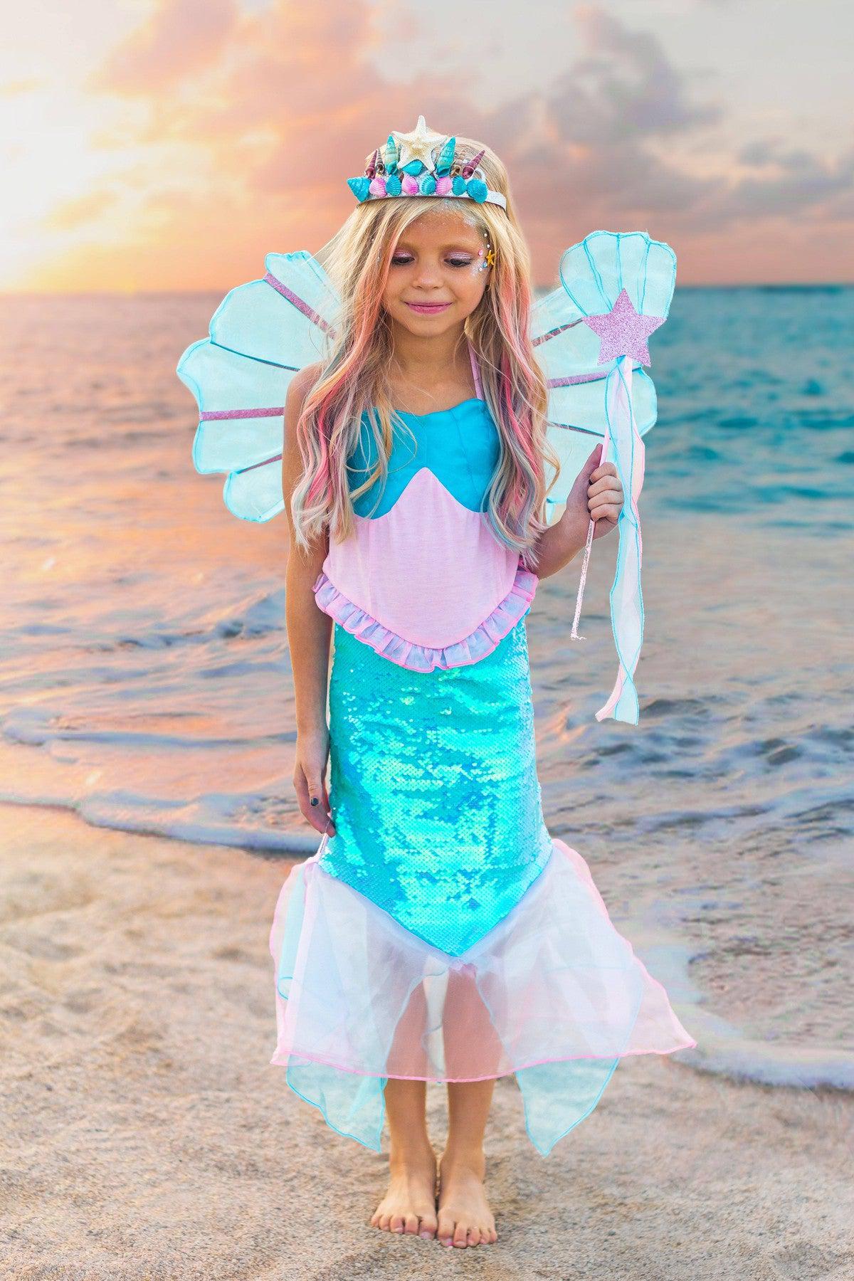 Deluxe Mermaid Costume - 4 Piece Complete Set! - XXS-12-18 Months - Child wearing blue and pink mermaid costume with iridescent tail, shell top, wings, crown, and trident on beach at sunset.