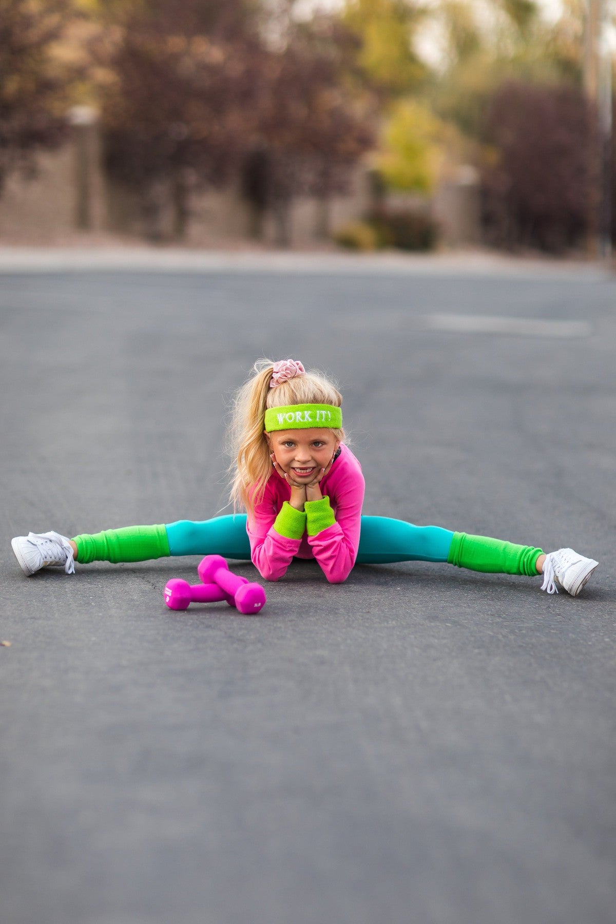 Mom & Me - '80s Workout Costume - COMPLETE SET! - CHILD-2XS-12-18 Months - Child wearing neon pink and green '80s workout costume with matching headband and pink dumbbells, stretching on pavement.