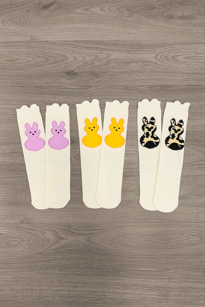 Peep Bunny Socks - Purple - Three pairs of cream-colored socks with scalloped cuffs, each featuring a playful bunny face in purple, yellow, and cheetah.
