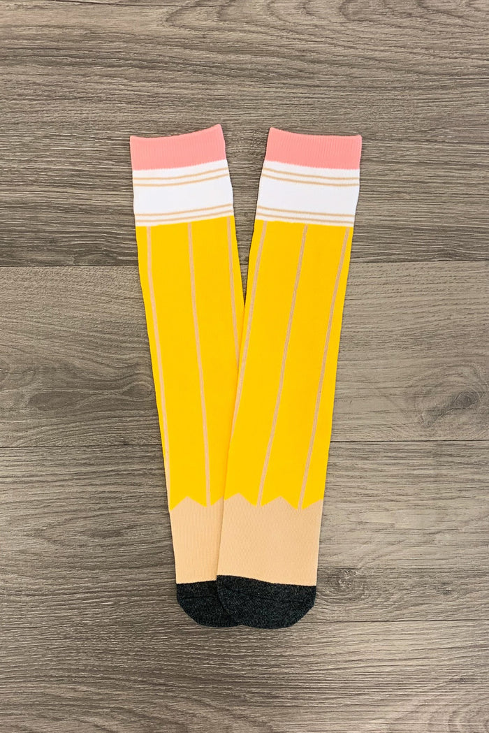 Pencil Knee High Socks - Default Title - Yellow pencil-themed knee-high socks with pink eraser, white bands, and black toe tips on wooden floor.
